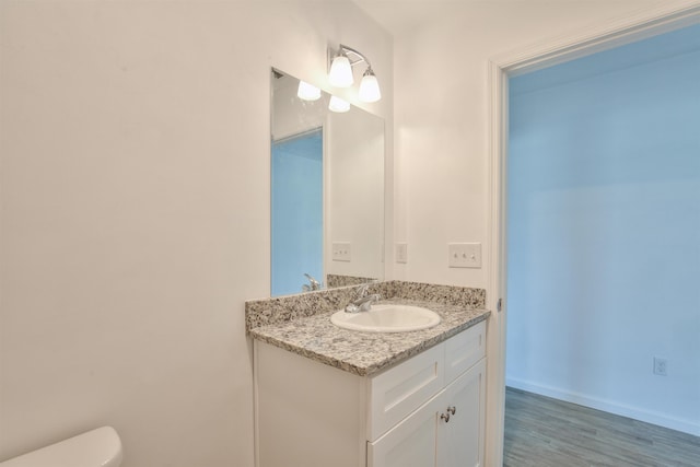 half bath featuring toilet, wood finished floors, vanity, and baseboards