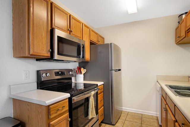 kitchen featuring appliances with stainless steel finishes, light countertops, brown cabinets, baseboards, and light tile patterned flooring