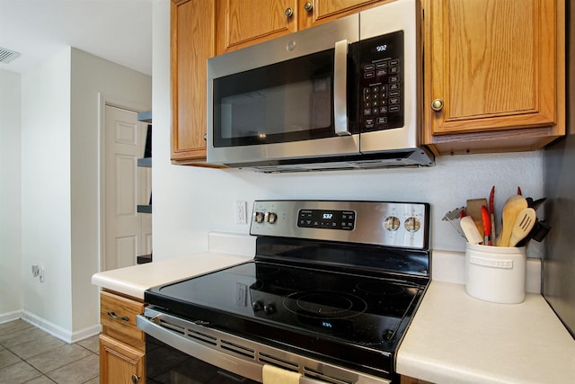 kitchen with appliances with stainless steel finishes, light countertops, light tile patterned floors, baseboards, and brown cabinets