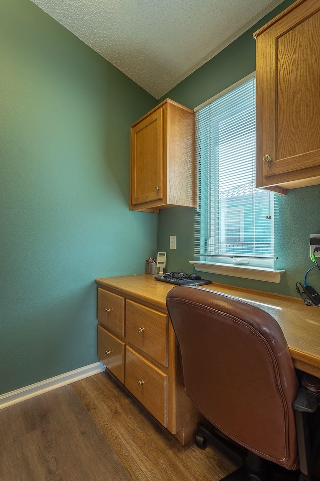 office featuring dark wood-type flooring, built in desk, and a textured ceiling