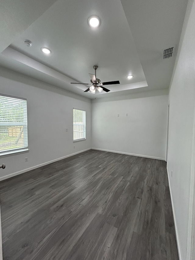unfurnished room featuring baseboards, a tray ceiling, visible vents, and dark wood finished floors