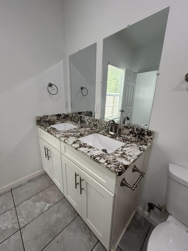 bathroom with toilet, a sink, double vanity, and baseboards