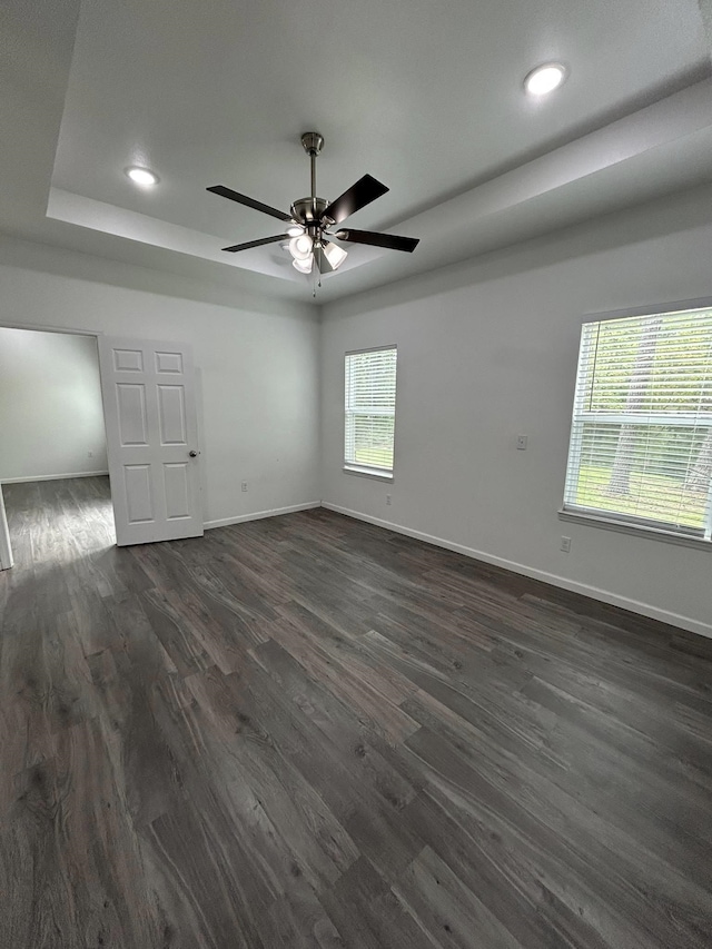 unfurnished room featuring baseboards, a tray ceiling, a ceiling fan, and dark wood finished floors