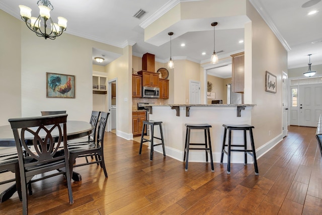 kitchen featuring visible vents, brown cabinets, stainless steel microwave, dark wood finished floors, and a breakfast bar area