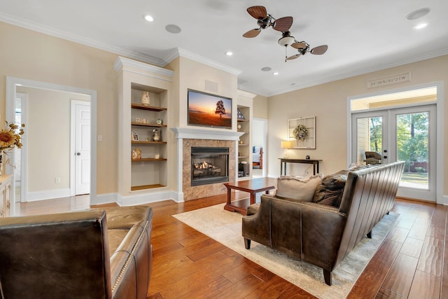 living area featuring hardwood / wood-style floors, baseboards, a tile fireplace, ceiling fan, and crown molding