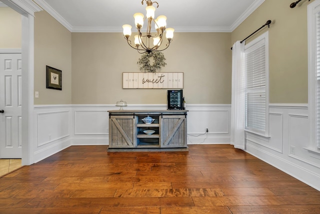 unfurnished dining area featuring hardwood / wood-style flooring, ornamental molding, a wainscoted wall, and a chandelier