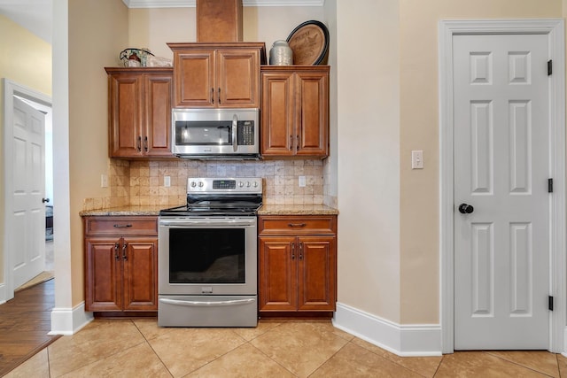 kitchen featuring backsplash, light stone counters, light tile patterned floors, and appliances with stainless steel finishes