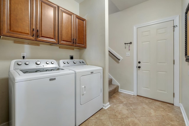 clothes washing area with cabinet space, light tile patterned floors, washer and dryer, and baseboards