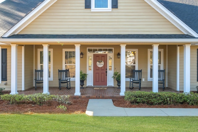 entrance to property featuring covered porch and roof with shingles