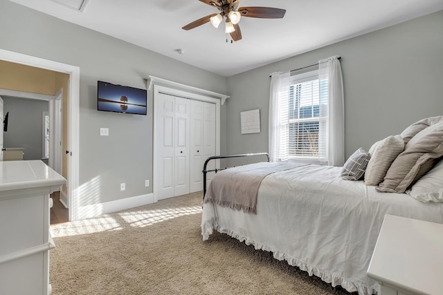 bedroom featuring light carpet, ceiling fan, baseboards, and a closet