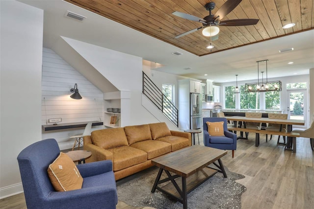 living room featuring ceiling fan with notable chandelier, wood-type flooring, lofted ceiling, wood ceiling, and wood walls