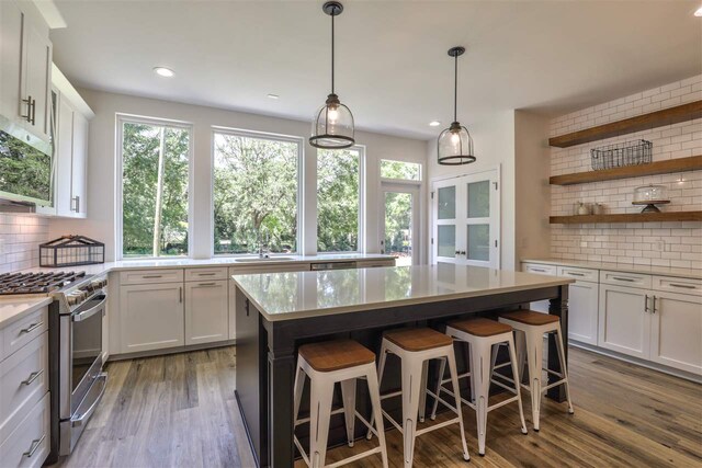 kitchen with white cabinetry, appliances with stainless steel finishes, hardwood / wood-style floors, hanging light fixtures, and decorative backsplash