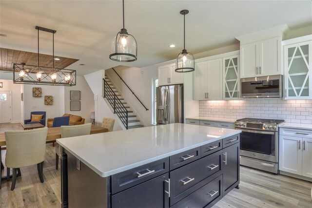 kitchen featuring a kitchen island, white cabinetry, appliances with stainless steel finishes, decorative light fixtures, and light hardwood / wood-style floors