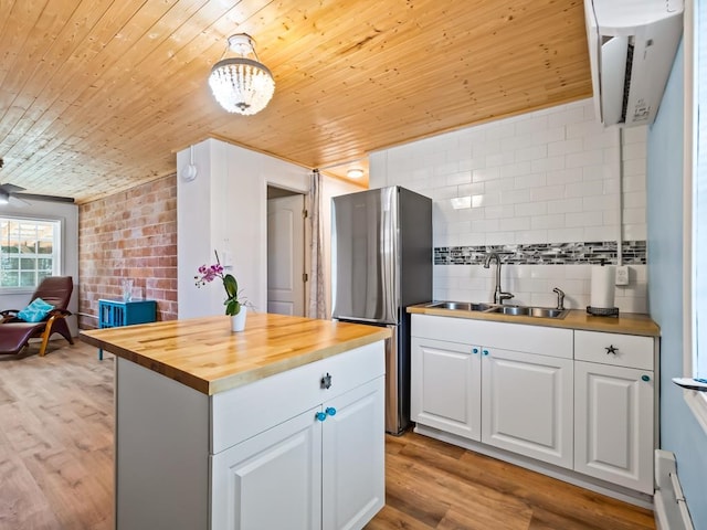 kitchen featuring white cabinets, sink, butcher block countertops, light hardwood / wood-style floors, and stainless steel refrigerator