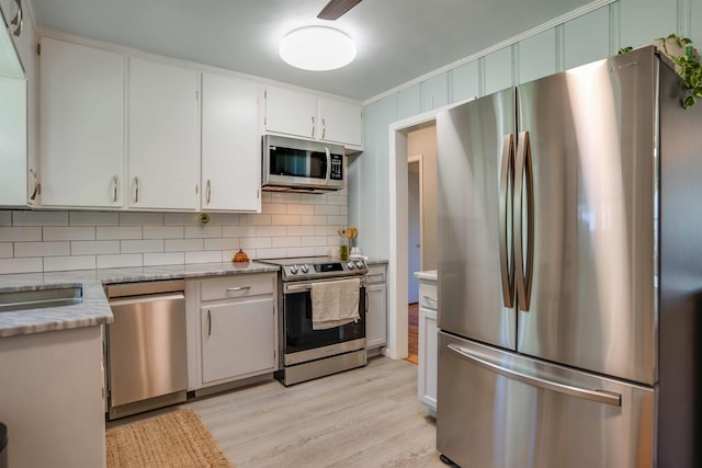 kitchen with appliances with stainless steel finishes, tasteful backsplash, white cabinetry, ornamental molding, and light wood-type flooring