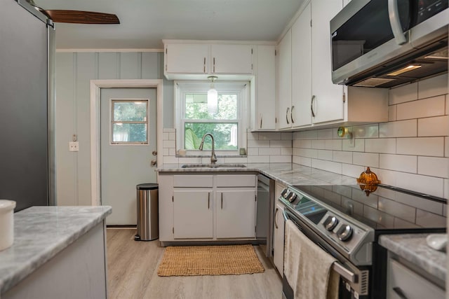 kitchen with sink, light wood-type flooring, white cabinets, and appliances with stainless steel finishes