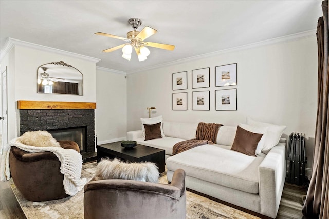 living area with ceiling fan, ornamental molding, a stone fireplace, and wood finished floors