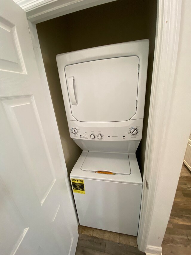 laundry room with dark wood-type flooring and stacked washer / drying machine