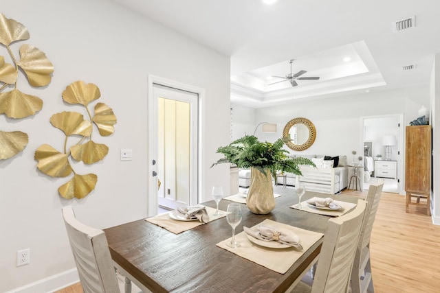 dining space with light wood-type flooring, a tray ceiling, and ceiling fan