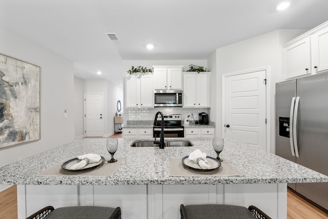 kitchen with white cabinets, a center island with sink, sink, a kitchen bar, and stainless steel appliances