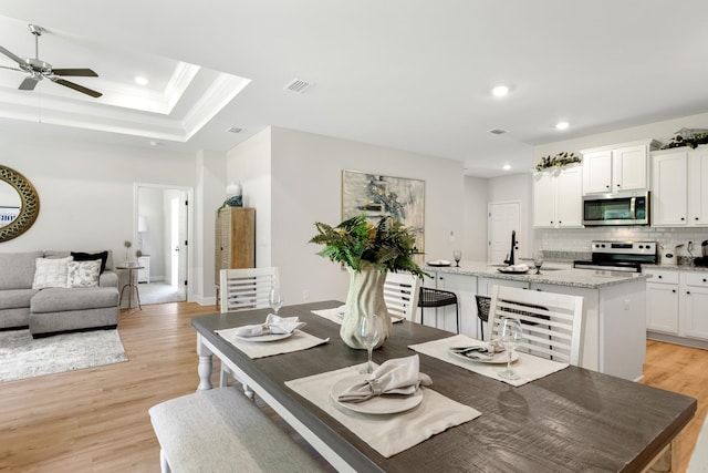 dining space with a tray ceiling, crown molding, ceiling fan, and light hardwood / wood-style floors