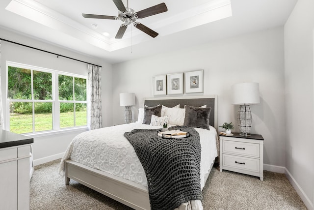 carpeted bedroom with a raised ceiling and ceiling fan