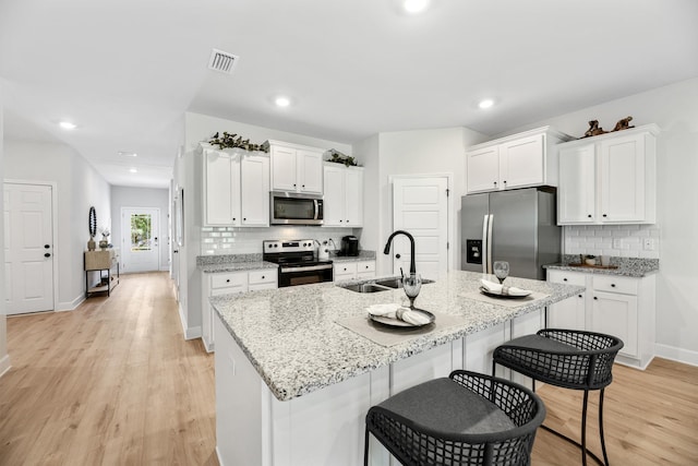 kitchen with light stone countertops, sink, an island with sink, white cabinets, and appliances with stainless steel finishes