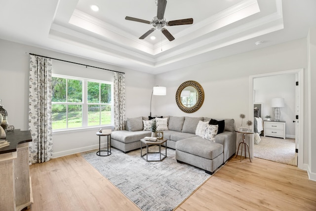 living room with a raised ceiling, ceiling fan, crown molding, and light wood-type flooring