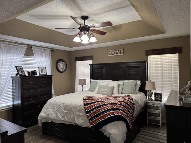 bedroom with ceiling fan, dark hardwood / wood-style flooring, a tray ceiling, and a textured ceiling