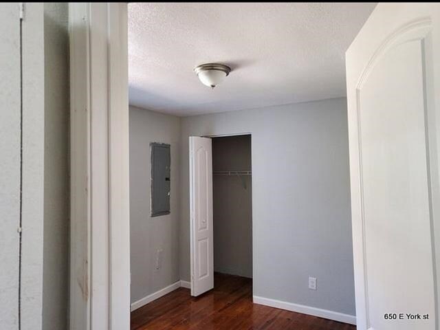 unfurnished bedroom with electric panel, a textured ceiling, and dark hardwood / wood-style floors