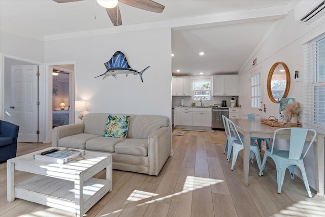 living room with a wall unit AC, light wood-type flooring, ceiling fan, sink, and lofted ceiling