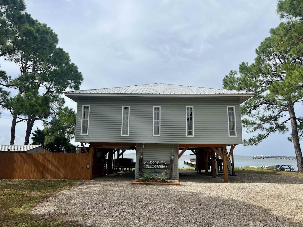 exterior space with metal roof, a water view, fence, driveway, and a carport