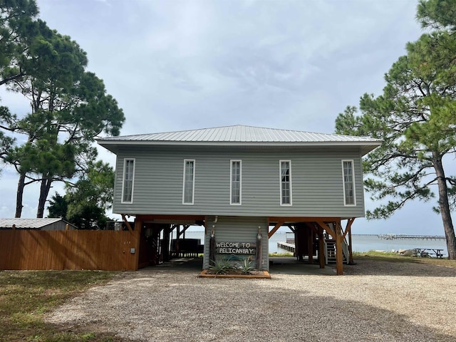 exterior space with metal roof, a water view, fence, driveway, and a carport