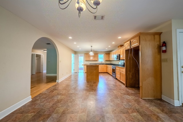 kitchen featuring appliances with stainless steel finishes, a textured ceiling, decorative light fixtures, a chandelier, and a kitchen island