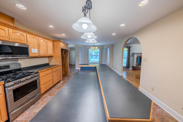 kitchen with appliances with stainless steel finishes, light brown cabinets, decorative light fixtures, and a notable chandelier