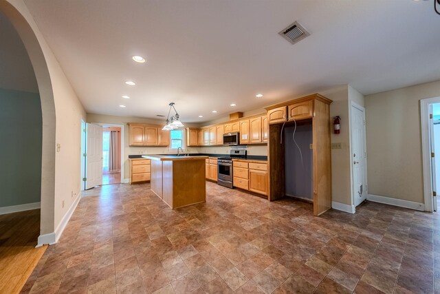 kitchen featuring appliances with stainless steel finishes, sink, light brown cabinets, pendant lighting, and a kitchen island