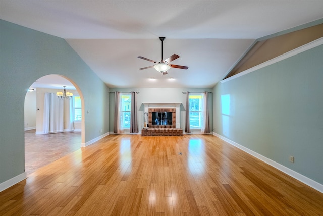 unfurnished living room with ceiling fan with notable chandelier, light hardwood / wood-style floors, lofted ceiling, and a brick fireplace