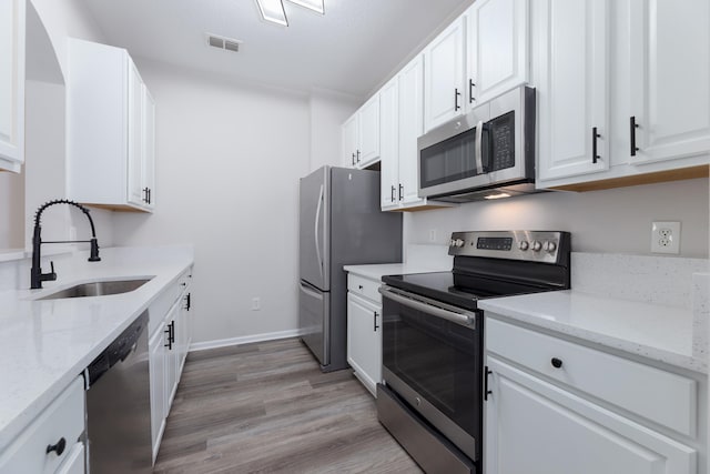 kitchen featuring sink, appliances with stainless steel finishes, light stone countertops, light hardwood / wood-style flooring, and white cabinets