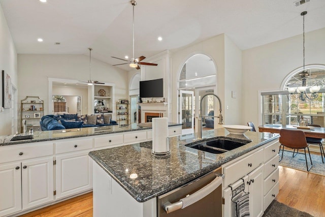 kitchen featuring sink, white cabinets, a center island with sink, stainless steel dishwasher, and dark stone counters