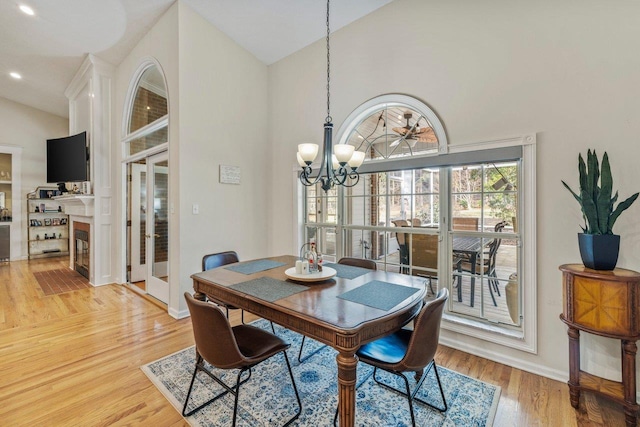 dining area with high vaulted ceiling, a notable chandelier, and light hardwood / wood-style floors