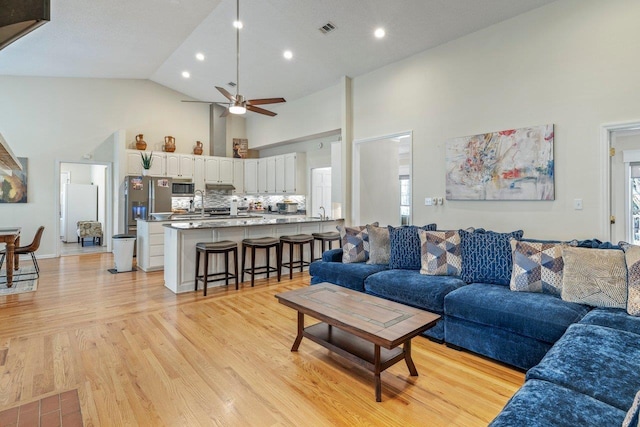 living room featuring ceiling fan, light wood-type flooring, and high vaulted ceiling