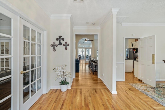 hall featuring crown molding, a textured ceiling, light wood-type flooring, and french doors