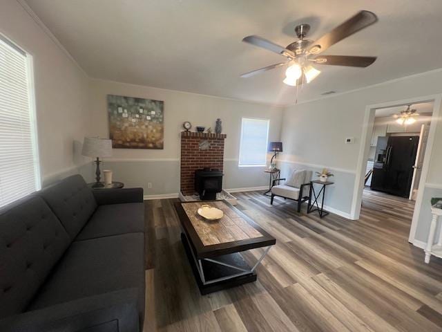 living room with ceiling fan, a wood stove, and wood-type flooring