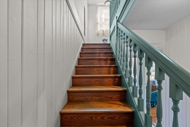 staircase featuring wood walls and a textured ceiling