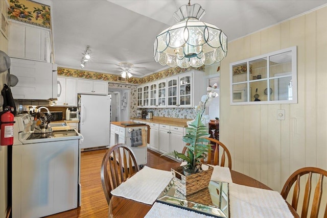 dining room with ceiling fan with notable chandelier, light hardwood / wood-style flooring, and wooden walls