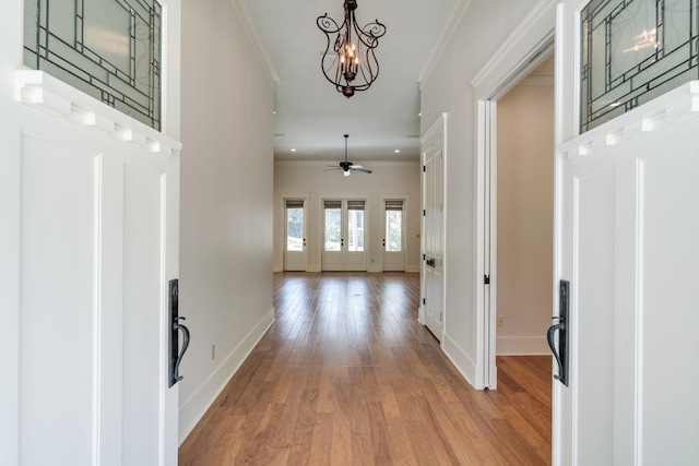 foyer featuring ornamental molding, ceiling fan with notable chandelier, baseboards, and wood finished floors