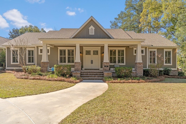 view of front of home with brick siding, a shingled roof, covered porch, board and batten siding, and a front lawn