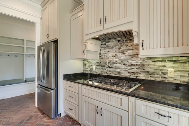 kitchen with tasteful backsplash, ornamental molding, brick floor, custom exhaust hood, and stainless steel appliances