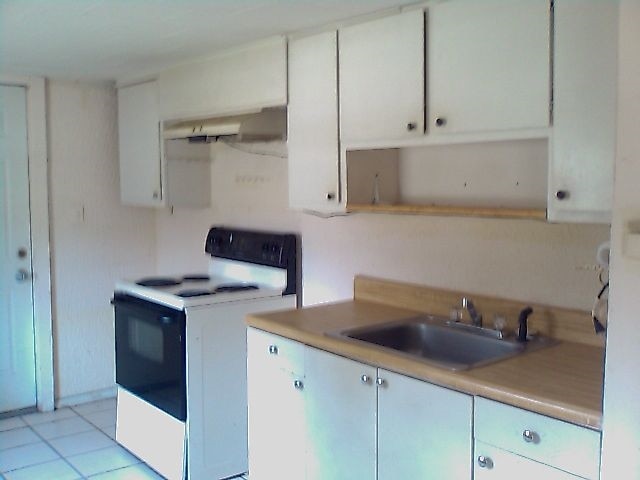 kitchen with white electric stove, sink, light tile patterned floors, and white cabinets