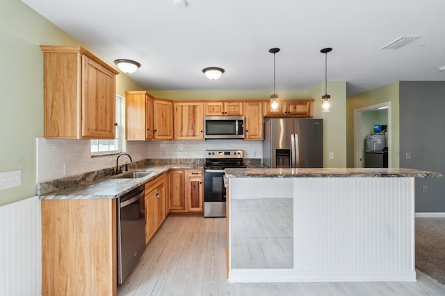 kitchen with sink, light hardwood / wood-style flooring, a kitchen island, pendant lighting, and stainless steel appliances